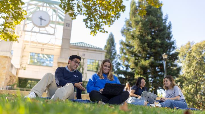 Students with laptops sitting on grass
